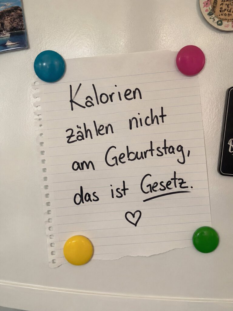 Handgeschriebener Zettel am Kühlschrank mit bunten Magneten: Kalorien zählen nicht am Geburtstag, das ist Gesetz